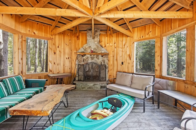 sunroom / solarium with lofted ceiling with beams, wood ceiling, and a stone fireplace