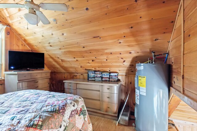 bedroom featuring water heater, vaulted ceiling, wood walls, light wood-type flooring, and ceiling fan