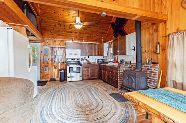 kitchen featuring a wood stove, wooden walls, vaulted ceiling with beams, stainless steel electric range, and ceiling fan