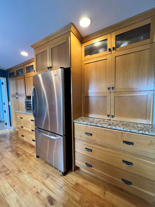 kitchen with light wood-type flooring, stainless steel fridge, and light stone counters