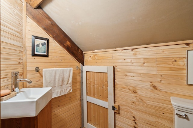 bathroom featuring lofted ceiling with beams, wooden walls, sink, and toilet