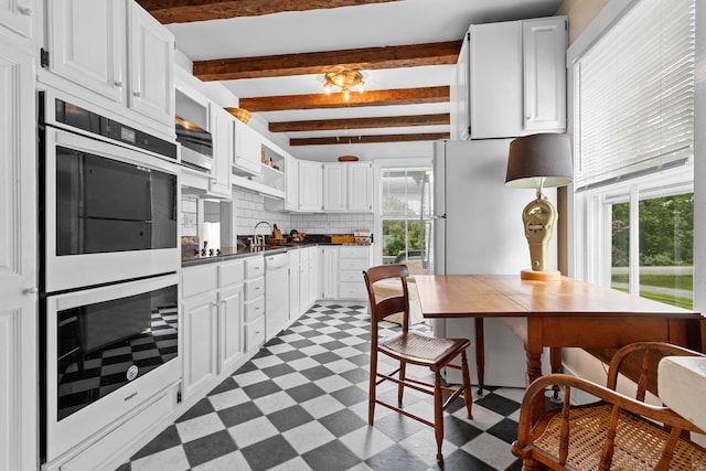 kitchen with appliances with stainless steel finishes, backsplash, beamed ceiling, and white cabinets