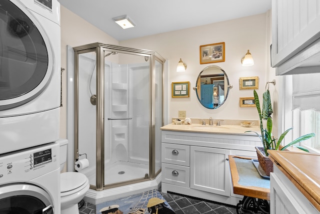 bathroom featuring vanity, toilet, stacked washer / drying machine, and a shower with door