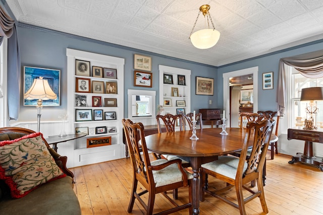 dining space with built in shelves, light wood-type flooring, and ornamental molding