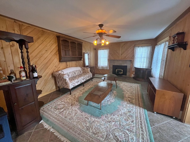 living room with ceiling fan, wooden walls, dark tile patterned flooring, and a tile fireplace