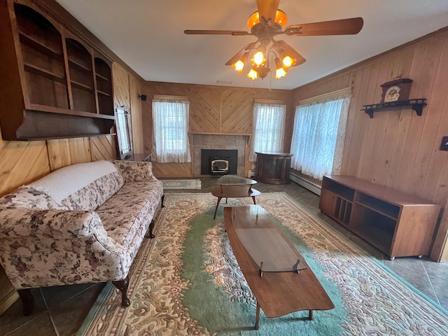 living room with ceiling fan, a baseboard heating unit, wood walls, and a tiled fireplace