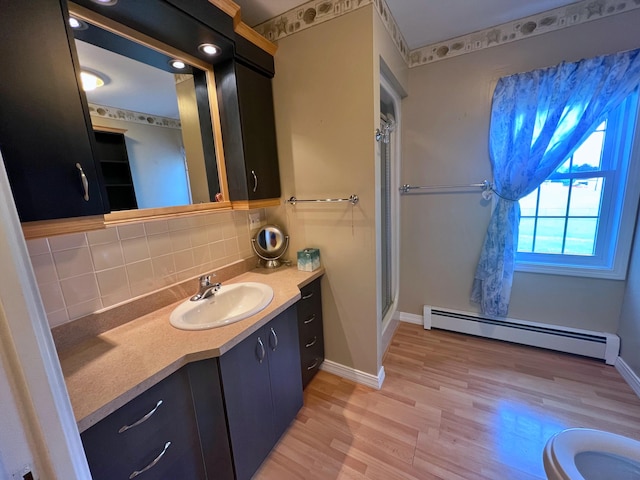 bathroom featuring decorative backsplash, a shower with shower door, vanity, baseboard heating, and hardwood / wood-style flooring