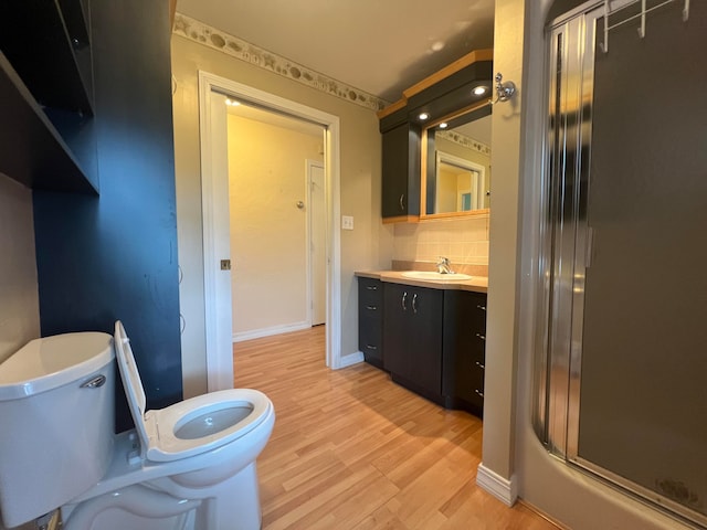 bathroom featuring vanity, hardwood / wood-style flooring, walk in shower, toilet, and decorative backsplash