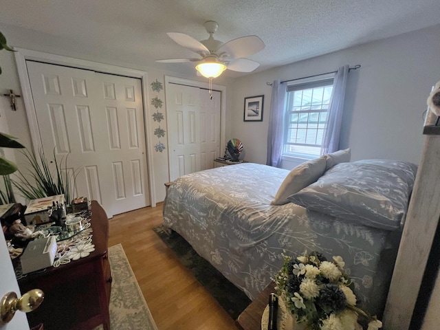 bedroom with light wood-type flooring, two closets, ceiling fan, and a textured ceiling