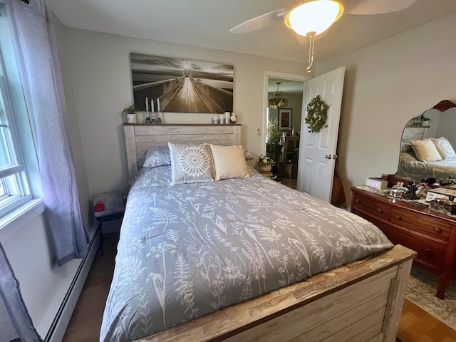 bedroom with ceiling fan, dark hardwood / wood-style floors, and a baseboard heating unit