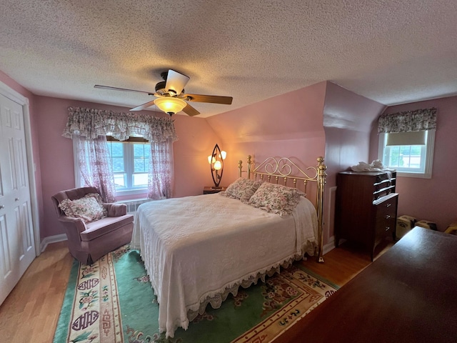 bedroom featuring vaulted ceiling, a closet, a textured ceiling, ceiling fan, and light hardwood / wood-style flooring