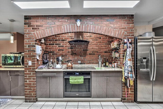 kitchen featuring light tile patterned floors, stainless steel appliances, brick wall, and wall chimney exhaust hood