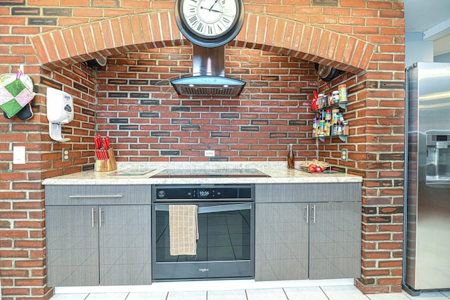 kitchen with light tile patterned flooring, gray cabinets, brick wall, stainless steel appliances, and light stone countertops