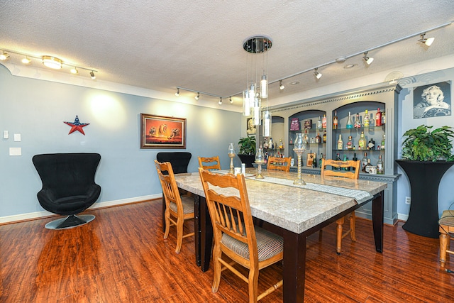 dining area featuring track lighting, dark wood-type flooring, bar area, and a textured ceiling