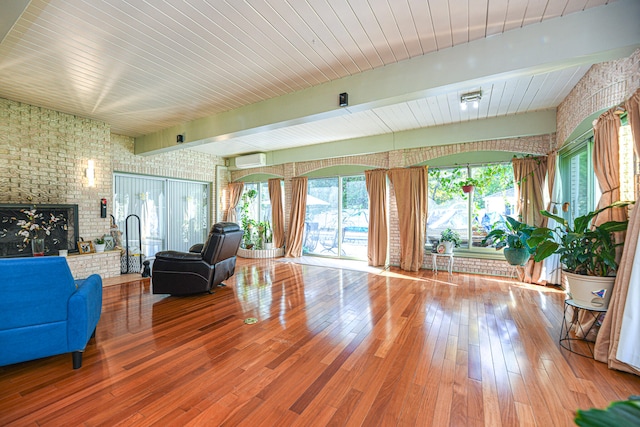 living room featuring hardwood / wood-style floors, beam ceiling, brick wall, a fireplace, and a wall mounted AC