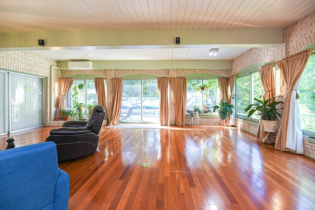 living room featuring brick wall, a wall mounted AC, hardwood / wood-style floors, and a healthy amount of sunlight