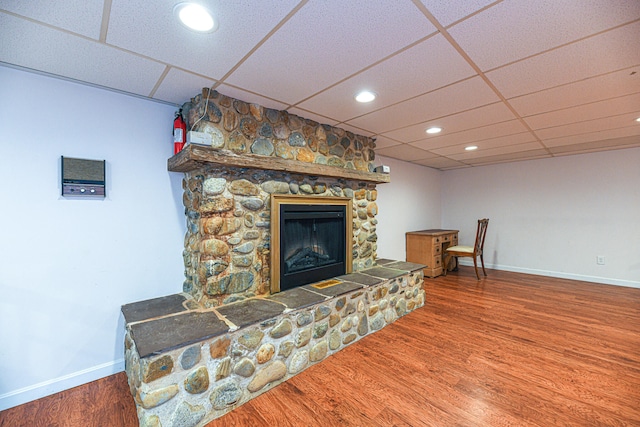 living room featuring wood-type flooring, a fireplace, and a drop ceiling