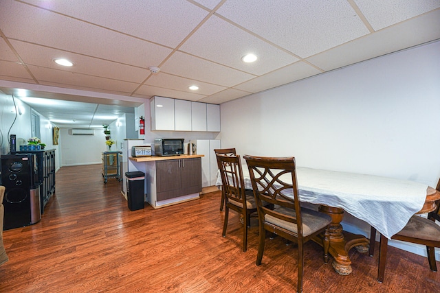 dining area with a wall mounted air conditioner, a drop ceiling, and dark hardwood / wood-style flooring