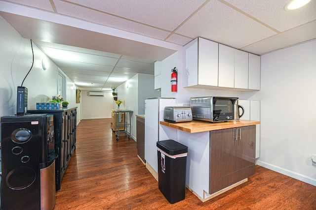 kitchen with white cabinets, a wall mounted AC, a drop ceiling, dark hardwood / wood-style floors, and wood counters