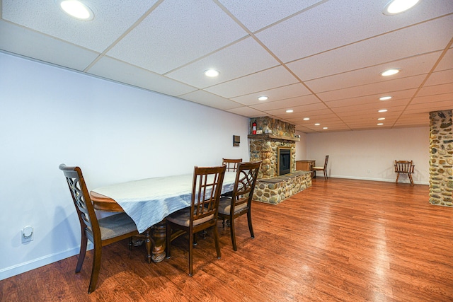 dining room with a stone fireplace, hardwood / wood-style flooring, and a paneled ceiling