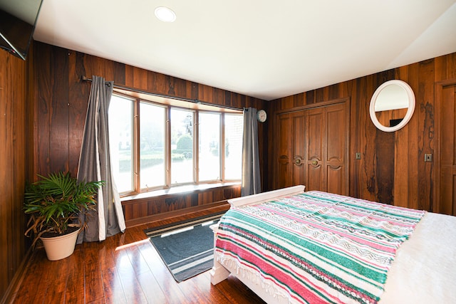 bedroom with wood walls, a closet, and dark hardwood / wood-style flooring