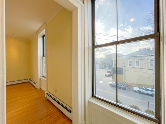 hallway featuring light hardwood / wood-style floors, baseboard heating, and ornamental molding