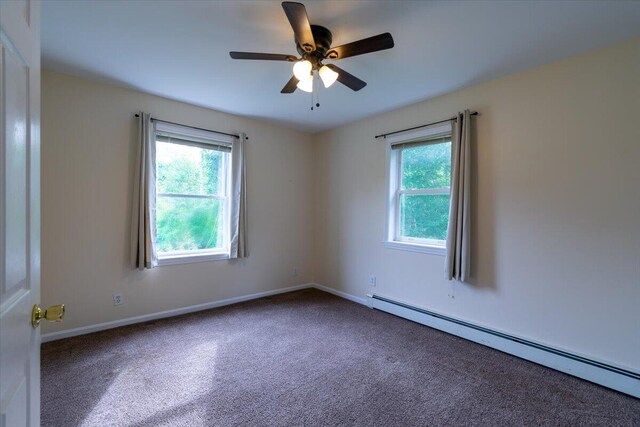 carpeted spare room featuring baseboard heating, ceiling fan, and plenty of natural light