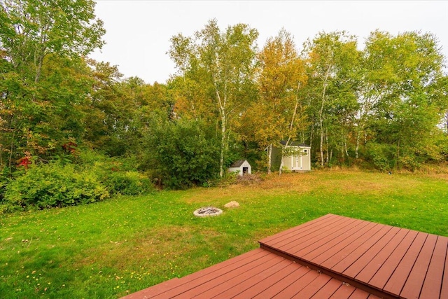 wooden deck with a lawn, a storage unit, and an outdoor fire pit