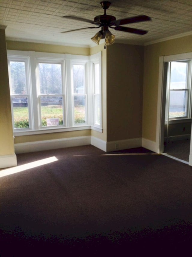 unfurnished room featuring crown molding, baseboards, ceiling fan, and dark carpet