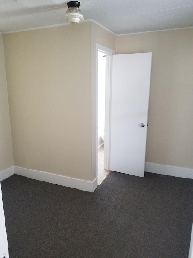 spare room with baseboards and dark carpet