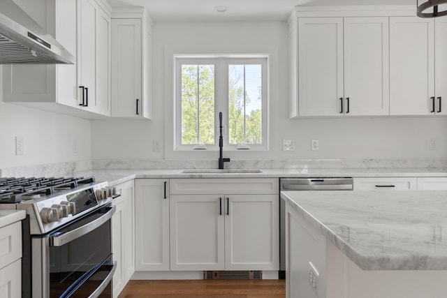 kitchen with light stone counters, sink, white cabinets, stainless steel stove, and wall chimney exhaust hood