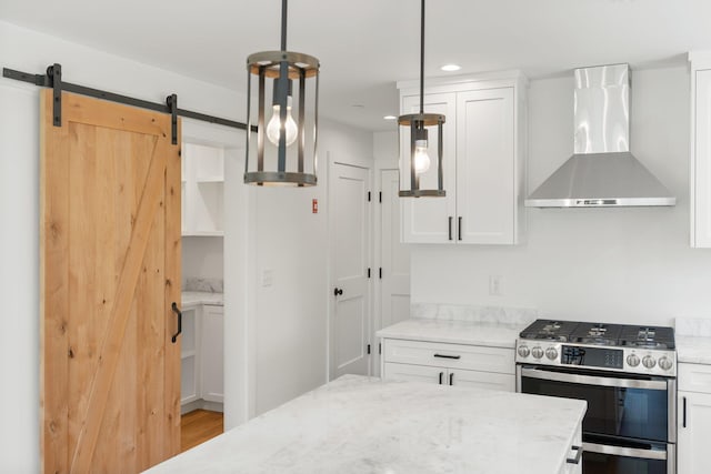 kitchen featuring hanging light fixtures, white cabinets, light stone countertops, wall chimney range hood, and stainless steel range