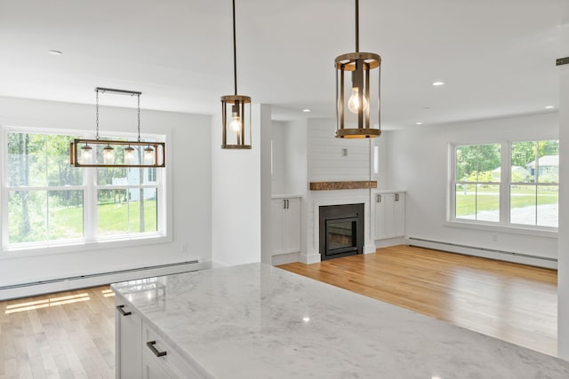 kitchen featuring plenty of natural light, white cabinetry, baseboard heating, decorative light fixtures, and light stone countertops