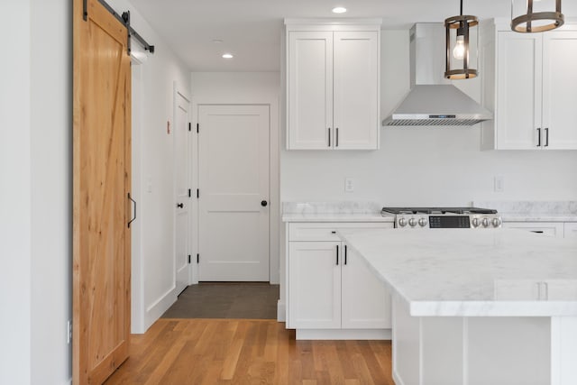 kitchen with pendant lighting, wall chimney range hood, white cabinetry, light wood-type flooring, and a barn door