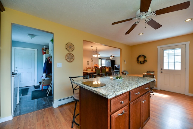 kitchen with light stone countertops, a baseboard radiator, a center island, a kitchen breakfast bar, and light hardwood / wood-style flooring