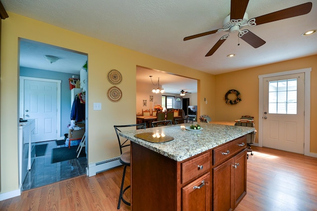 832 College St, Lewiston, ME 04240 - kitchen featuring a ceiling fan, a baseboard heating unit, a breakfast bar area, light wood finished floors, and plenty of natural light