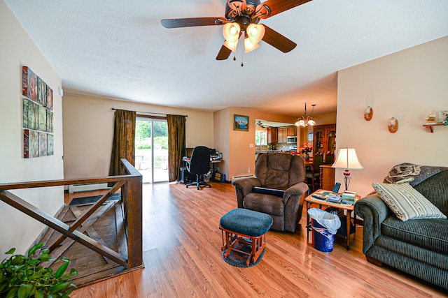 living room featuring light hardwood / wood-style floors, a textured ceiling, and ceiling fan with notable chandelier