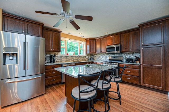 kitchen with light stone counters, a breakfast bar area, stainless steel appliances, light hardwood / wood-style floors, and a center island