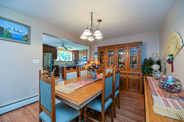 dining room with a textured ceiling, a baseboard radiator, light wood-type flooring, and ceiling fan with notable chandelier