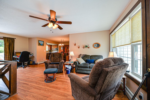 living room with light hardwood / wood-style floors, baseboard heating, plenty of natural light, and ceiling fan with notable chandelier