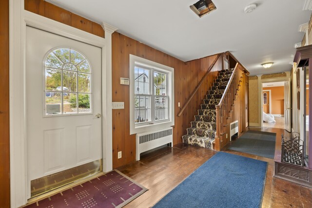 foyer entrance with wood-type flooring, radiator, and wood walls