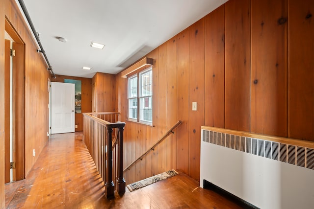 hallway featuring wood-type flooring, radiator, wood walls, and a barn door