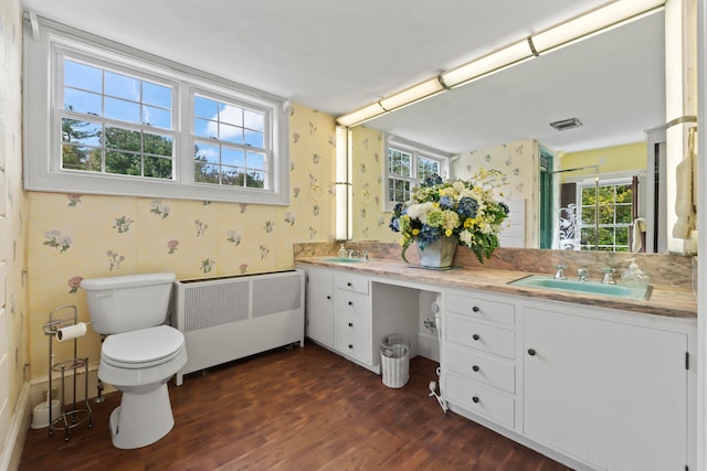 bathroom with radiator heating unit, a healthy amount of sunlight, hardwood / wood-style floors, and toilet