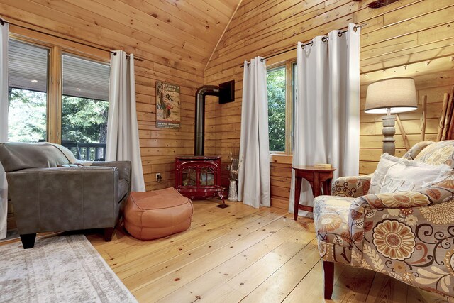 living area featuring a wood stove, wooden walls, vaulted ceiling, light hardwood / wood-style floors, and wood ceiling