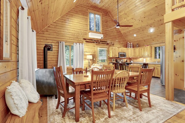 dining space with wood walls, a wood stove, high vaulted ceiling, ceiling fan, and wood ceiling