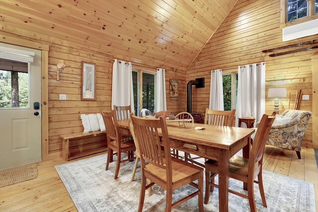 dining area featuring a wood stove, light hardwood / wood-style flooring, wooden walls, and wooden ceiling