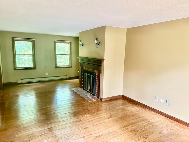 unfurnished living room featuring a textured ceiling, baseboard heating, a fireplace, and light hardwood / wood-style floors