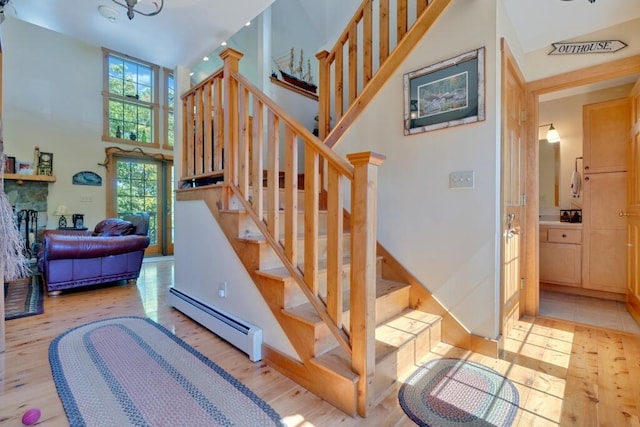 staircase featuring a baseboard radiator, a towering ceiling, hardwood / wood-style floors, and a stone fireplace