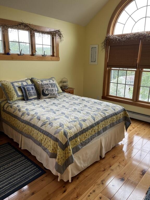 bedroom with a baseboard heating unit, light wood-type flooring, and multiple windows