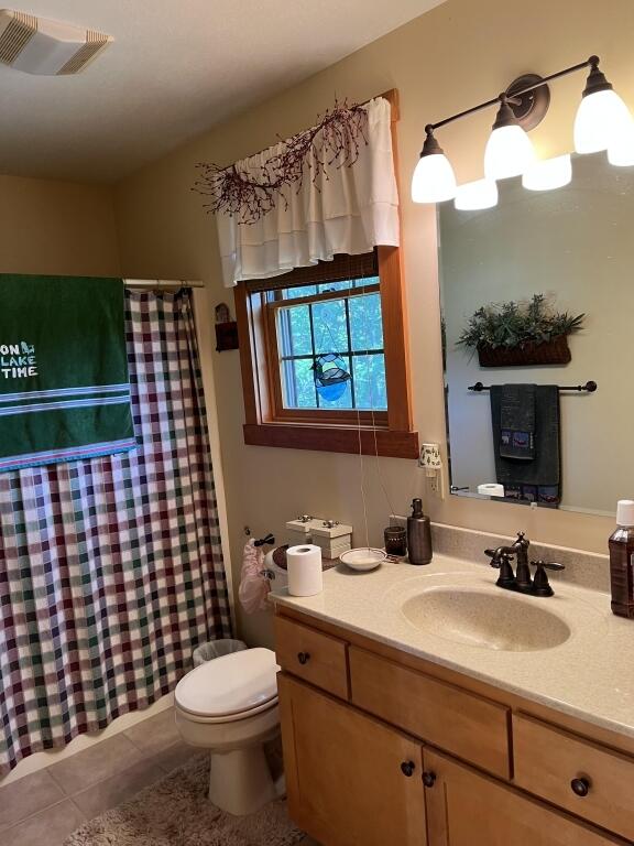 bathroom with tile patterned floors, walk in shower, vanity, and toilet